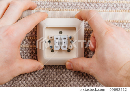 male hand replaces or repairs the light switch on the wall with brown wallpaper. 99692312