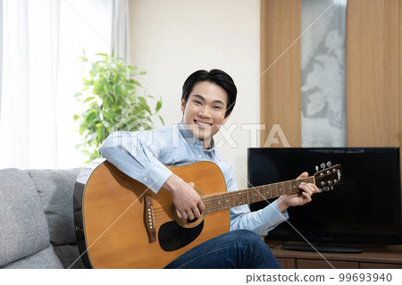 Man sitting on sofa playing guitar and smiling 99693940