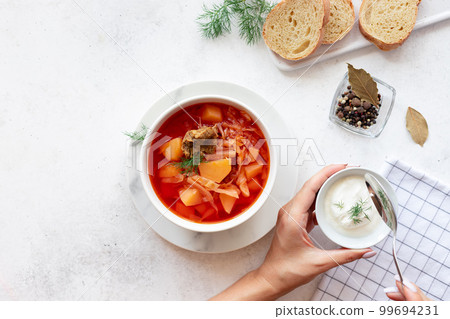 woman's hands put sour cream in a bowl with red borscht soup 99694231