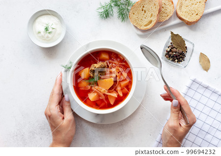 woman eating red borscht with vegetables, dill and meat. 99694232
