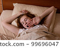 A young teenage girl is tired and yawns lying in bed 99696047
