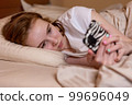 A young teenage girl lies in bed with a phone in her hands and watches social networks 99696049