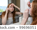 Teenage girl plucks her eyebrows looking in the mirror. High quality photo 99696051