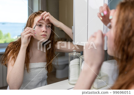 Teenage girl plucks her eyebrows looking in the mirror. High quality photo 99696051