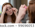 Teenage girl plucks her eyebrows looking in the mirror. High quality photo 99696053