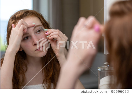 Teenage girl plucks her eyebrows looking in the mirror. High quality photo Teenage girl plucks her eyebrows looking in the mirror. High quality photo 99696053