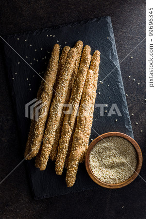 Italian grissini bread sticks with sesame seeds on black table. Top view. 99696345