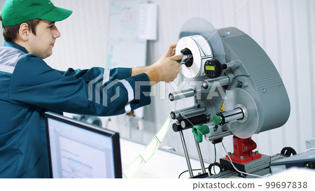 The worker changes paper roll with marking stickers on a machine with automated marking. 99697838
