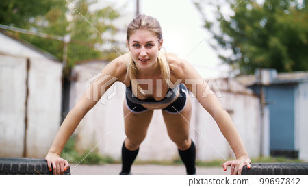 sexy athletic young blond woman in shorts, performs various strength exercises with the help of tires, push-ups, In summer, near old abandoned garages sexy athletic young blond woman in shorts, performs various strength exercises with the help of tires, push-ups, In summer, near old abandoned garages 99697842