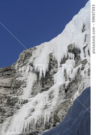 Icefall on steep rocky rocks against the blue sky in winter. 99697893
