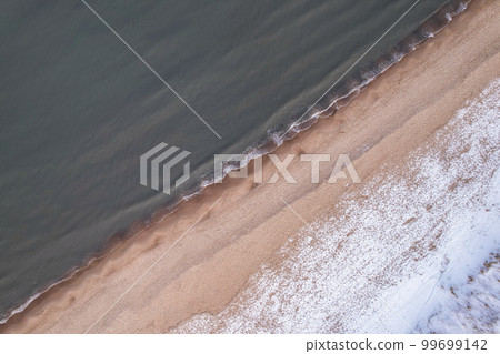 Winter in cold Baltic sea snowy beach in Gdansk. Aerial view of snow covered beach and dunes and dark calm sea nature landscape captured with drone. Tourism in Poland 99699142