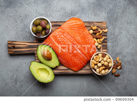 Food sources of healthy unsaturated fat: fresh raw salmon fillet, avocado, olives, nuts on cutting board, rustic stone background top view. Omega 3 and oil products, healthy nutrition and keto diet Food sources of healthy unsaturated fat: fresh raw salmon fillet, avocado, olives, nuts on cutting board, rustic stone background top view. Omega 3 and oil products, healthy nutrition and keto diet 99699304