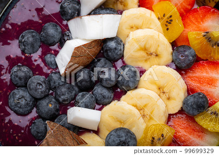 Healthy summer acai smoothie bowl with chia seeds, fresh banana, strawberry, blueberry, cocos, kiwi top view, rustic concrete background with spoon 99699329