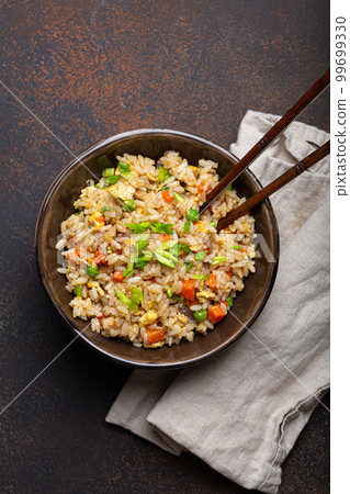 Authentic Chinese and Asian fried rice with egg and vegetables in ceramic brown bowl top view, dark rustic concrete table background. Traditional dish of China 99699330