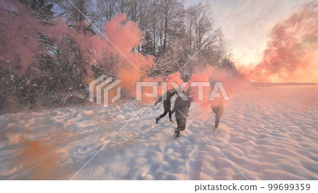 Girls friends run across the winter field with colored smoke. Girls friends run across the winter field with colored smoke. 99699359