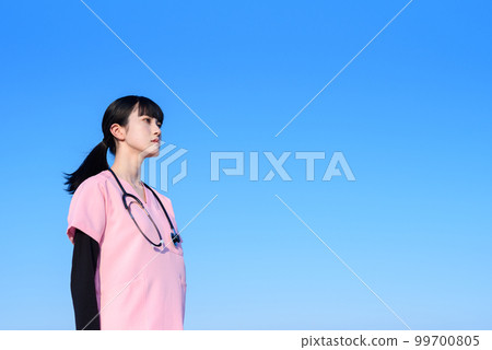 A female nurse wearing a scrub standing against the blue sky, a medical worker, a doctor, an outpatient, a medical examination, a future, a serious face 99700805