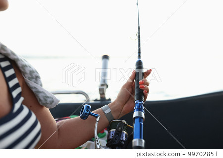 Female sitting in boat and holding fish rod in hands Female sitting in boat and holding fish rod in hands 99702851