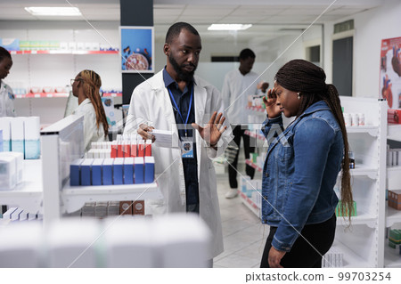 Customer buying headache medication, pharmacy consultant recommending buyer painkiller. African american woman suffering from migraine, standing in drugstore, chatting with pharmacist Customer buying headache medication, pharmacy consultant recommending buyer painkiller. African american woman suffering from migraine, standing in drugstore, chatting with pharmacist 99703254