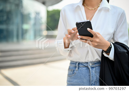 Cropped image of a gorgeous Asian businesswoman using her smartphone while walking on the street 99703297