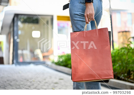 Cropped, a fashionable girl in jeans walking down a shopping street while holding shopping bags 99703298