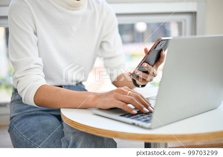 an Asian woman using her smartphone and laptop, remote working at the coffee shop. 99703299