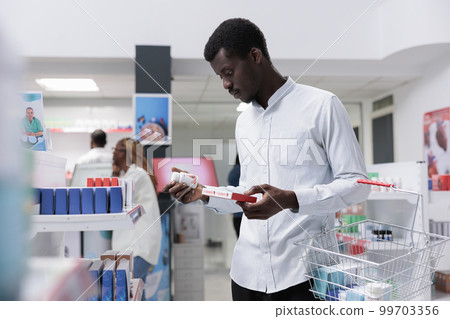 African american man checking food supplements in drugstore shelf, reading instruction on tablets package. Client choosing vitamins, buying prescription medications, side view African american man checking food supplements in drugstore shelf, reading instruction on tablets package. Client choosing vitamins, buying prescription medications, side view 99703356