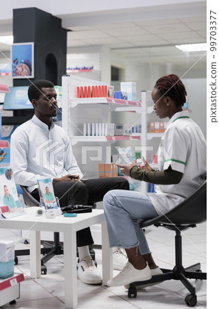 Pharmacist consultation, drugstore seller advising medicaments, holding pills package. African american man and medic talking, chemist and client communication, all black team 99703377