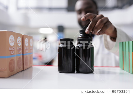 African american pharmacist taking medication from drugstore shelf closeup, selective focus on bottles. Pharmacy medic putting pills close up, vitamins selling, chemist front view 99703394