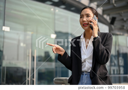 Professional Asian businesswoman is on the phone with business partner at outside of the building. Professional Asian businesswoman is on the phone with business partner at outside of the building. 99703958