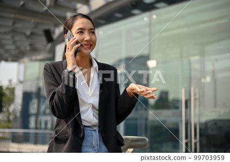 Successful Asian businesswoman is on the phone while walking outside along the company building Successful Asian businesswoman is on the phone while walking outside along the company building 99703959