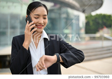Successful Asian female CEO is on the phone and checking the time on her wristwatch while walking Successful Asian female CEO is on the phone and checking the time on her wristwatch while walking 99703960
