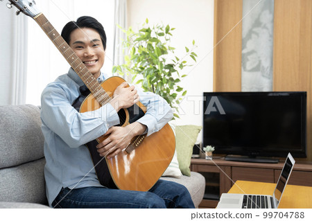 拿著吉他坐在沙發上微笑的男人 99704788