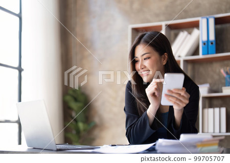Asian businesswoman using smartphone to do accounting work with laptop and graph of financial reports in office Asian businesswoman using smartphone to do accounting work with laptop and graph of financial reports in office 99705707