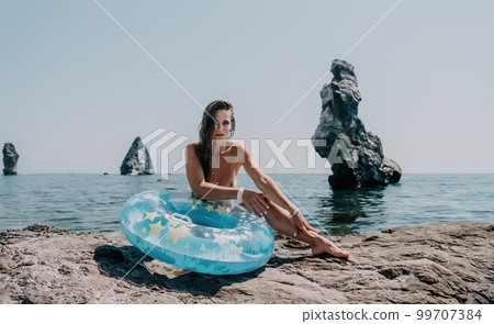 Woman summer sea. Happy woman swimming with inflatable donut on the beach in summer sunny day, surrounded by volcanic mountains. Summer vacation concept. Woman summer sea. Happy woman swimming with inflatable donut on the beach in summer sunny day, surrounded by volcanic mountains. Summer vacation concept. 99707384