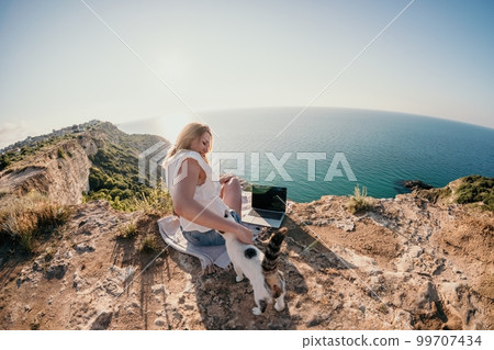Woman sea laptop. Business woman petting cat and working on laptop by the sea. Close up on hands of pretty lady typing on computer outdoors summer day. Freelance, digital nomad and holidays concept. Woman sea laptop. Business woman petting cat and working on laptop by the sea. Close up on hands of pretty lady typing on computer outdoors summer day. Freelance, digital nomad and holidays concept. 99707434