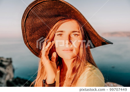 Portrait of happy young woman wearing summer black hat with large brim at beach on sunset. Closeup face of attractive girl with black straw hat. Happy young woman smiling and looking at camera at sea. 99707449