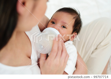 mother feeding milk bottle to her newborn baby on bed mother feeding milk bottle to her newborn baby on bed 99707714