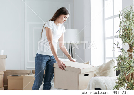 young woman opening a box in a new apartment young woman opening a box in a new apartment 99712363