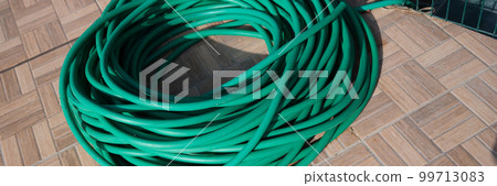 Green twisted garden hose in garden closeup 99713083