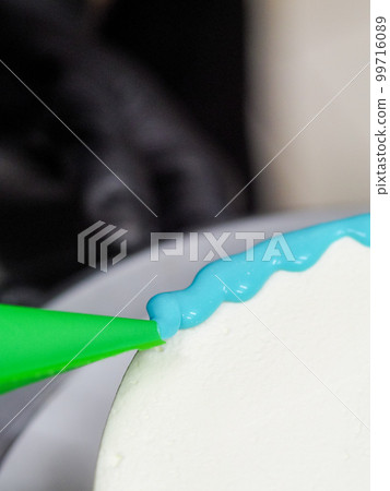 hand pastry chef designer topping a frosted white cake with pastel light blue drip filling bag hand pastry chef designer topping a frosted white cake with pastel light blue drip filling bag 99716089