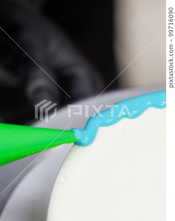 hand pastry chef designer topping a frosted white cake with pastel light blue drip filling bag hand pastry chef designer topping a frosted white cake with pastel light blue drip filling bag 99716090