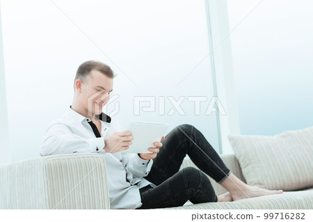smiling man with digital tablet sitting on sofa in his living room 99716282