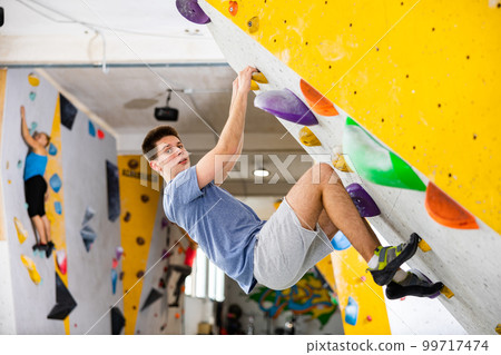 Male mountaineer climbing artificial rock wall without his belay indoors Male mountaineer climbing artificial rock wall without his belay indoors 99717474