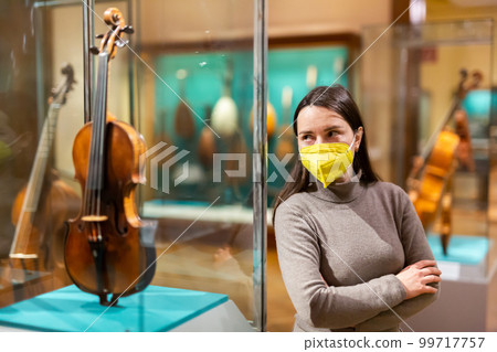 Woman in mask viewing collections of ancient musical instruments in museum 99717757