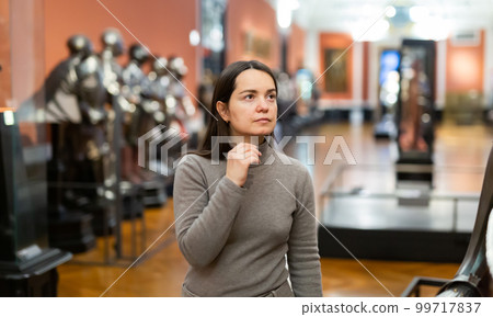 Female museum visitor examining with interest ancient armor 99717837