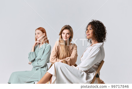 Group portrait of different beautiful young women in elegant dresses sitting on chairs over light background. Concept of beauty, fashion, business, ad Group portrait of different beautiful young women in elegant dresses sitting on chairs over light background. Concept of beauty, fashion, business, ad 99717846
