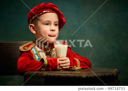 Tasting milk cocktail. Little charming kid in historical costume drinking milkshake over dark green background. Concept of fast food, comparison of eras, retro, vintage, emotions Tasting milk cocktail. Little charming kid in historical costume drinking milkshake over dark green background. Concept of fast food, comparison of eras, retro, vintage, emotions 99718733