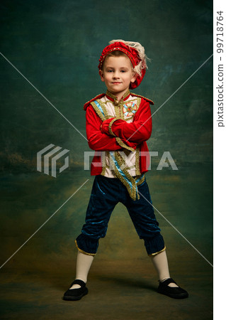 Portrait of cute little boy dressed up as medieval character, little prince and pageboy posing over dark vintage style background, Fashion, emotions, theater art concept Portrait of cute little boy dressed up as medieval character, little prince and pageboy posing over dark vintage style background, Fashion, emotions, theater art concept 99718764