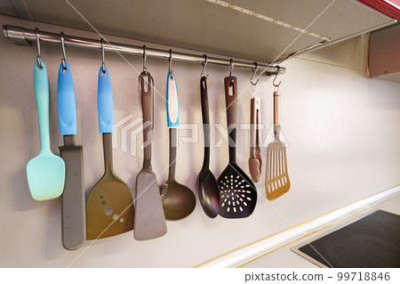 cutlery for cooking on hooks in the kitchen.  99718846