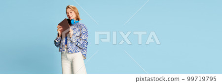 Beautiful happy young girl, student in headphones and casual clothes posing with tablet over blue studio background. Banner 99719795